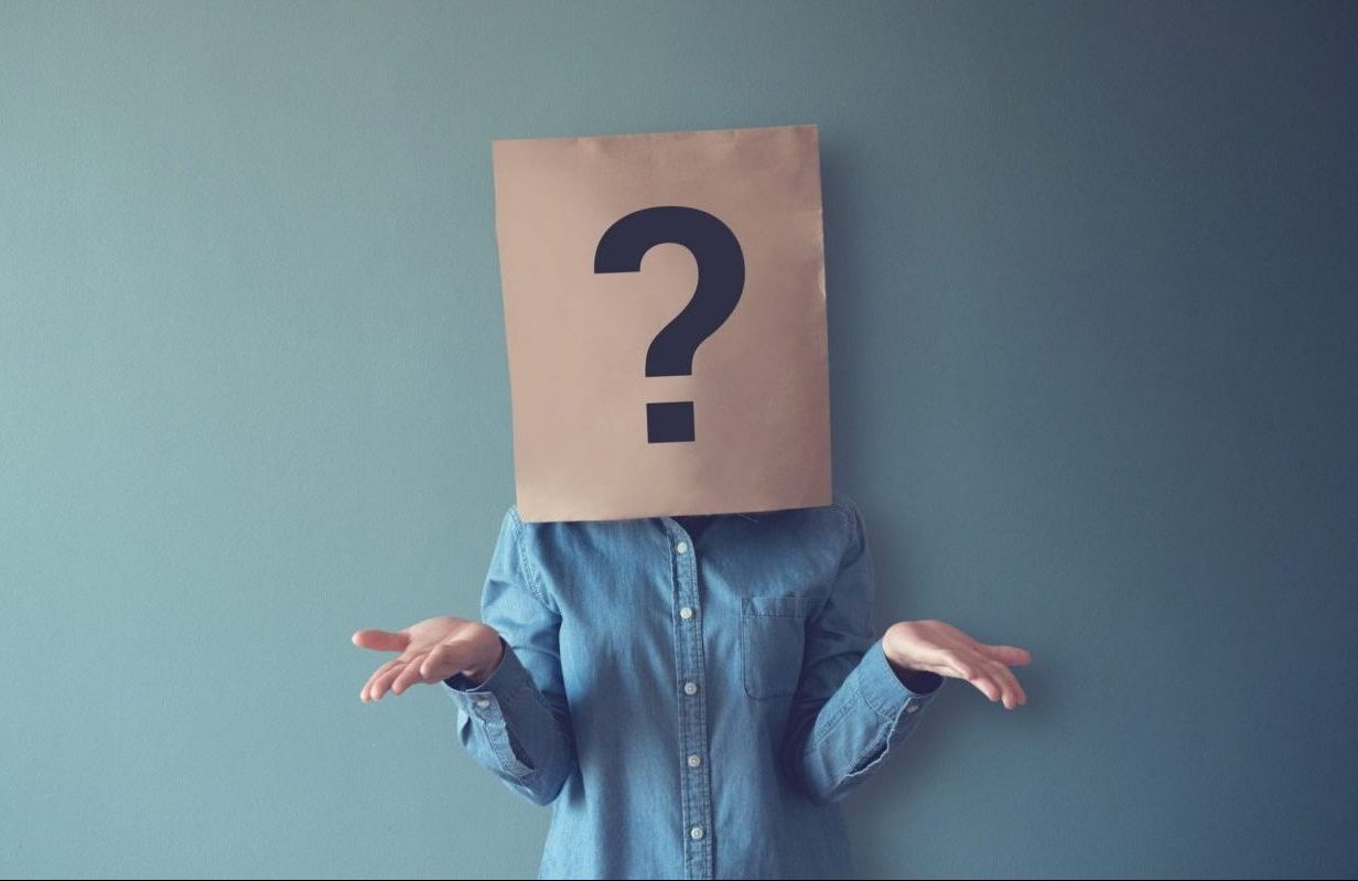 woman wears paperbag over her head with giant question mark