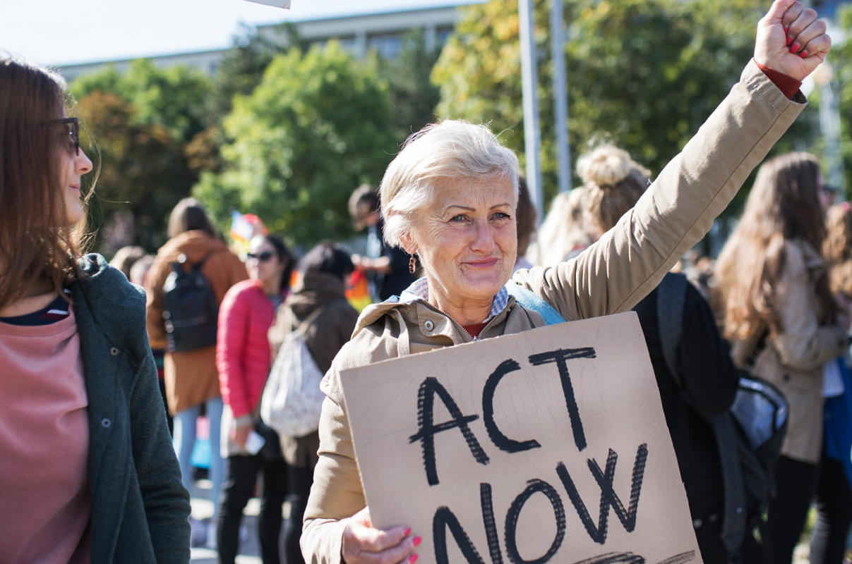 senior woman carries an "act now" sign during a protest