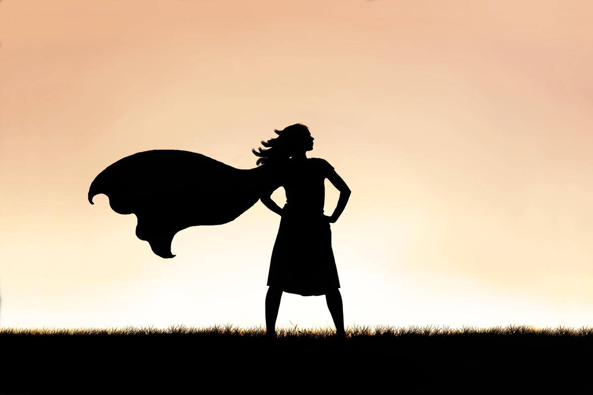 silhouette of a woman in a strong pose wearing a superhero cape against a sunset