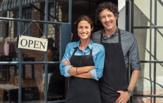 older couple as small business owners stand in front of their open store