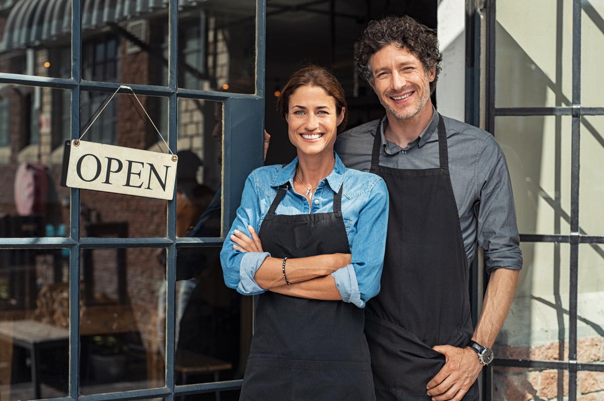 older couple as small business owners stand in front of their open store