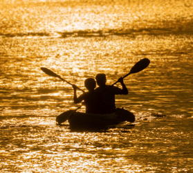 mature couple kayak at sunset on the ocean for healthy exercise
